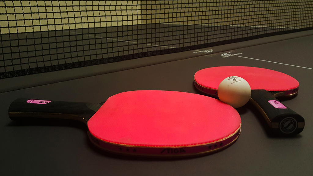 Zwei Tischtennisschläger mit Tischtennisball liegen auf der Platte.